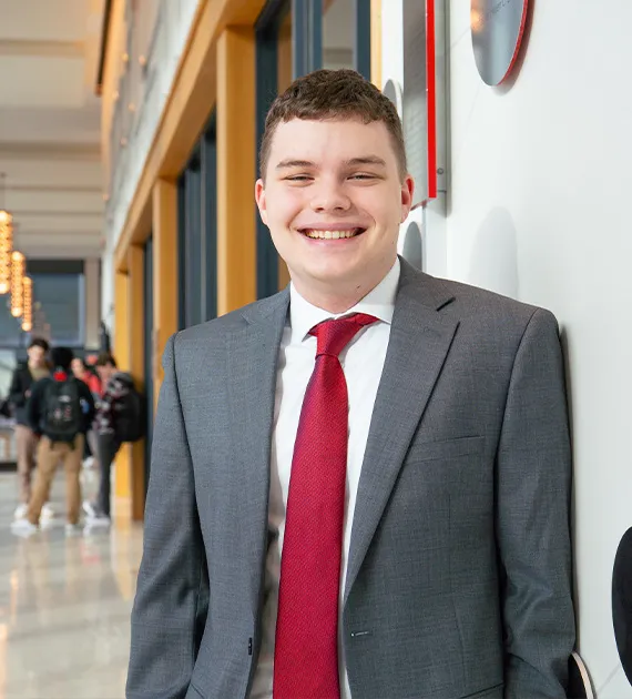 A male student with a gray suit and red tie smiling.