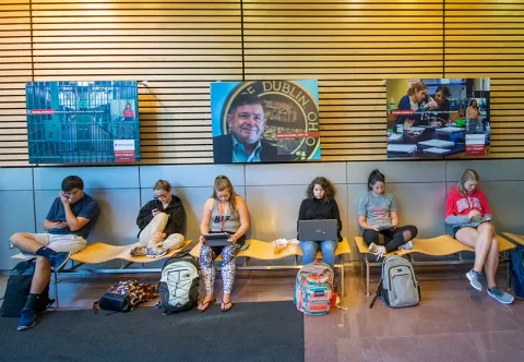 students sit on bench with laptops and books