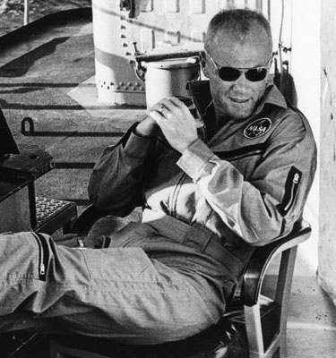 John Glenn seated with feet up relaxing aboard a ship