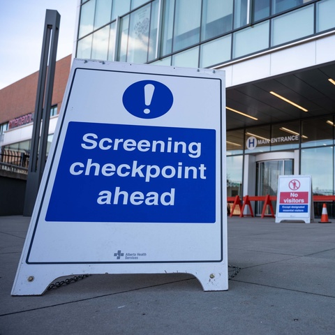 Blue and white sign that says "Screening checkpoint ahead" in front of a hospital entrance