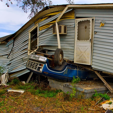 Blue vehicle upside down under gray home after a hurricane