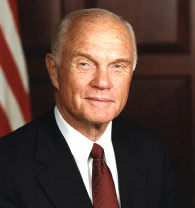 head and shoulders photo of John Glenn with U.S. flag in background