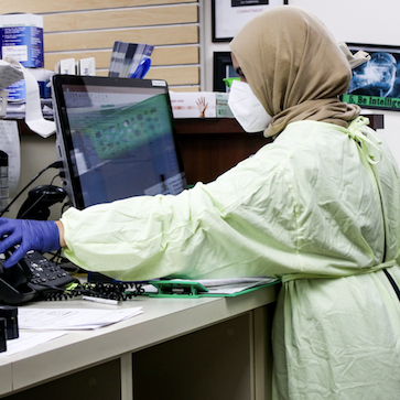 woman in hijab and PPE in front of computer