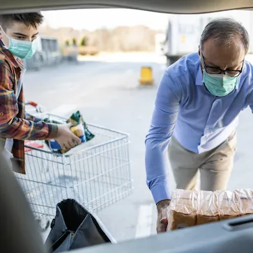 two individuals in masks load groceries into a car