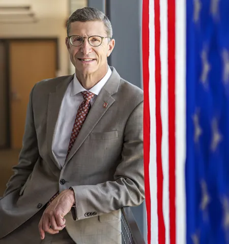 a man in a suit (Trevor Brown) in the background with an American flag in the foreground 