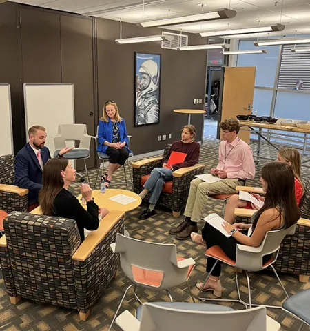 three adults and four high school students sit inside in a circle talking