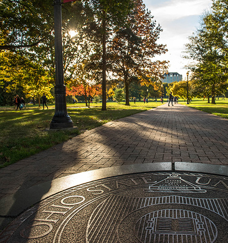  sunny day with fall trees on the Ohio State Oval looking west toward Thompson Library with the Ohio State University seal in the brick pathway in the foreground
