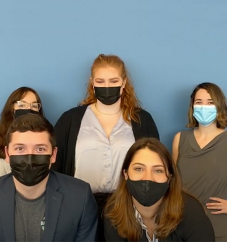 A group photo of five students with masks posed in front of a blue background.