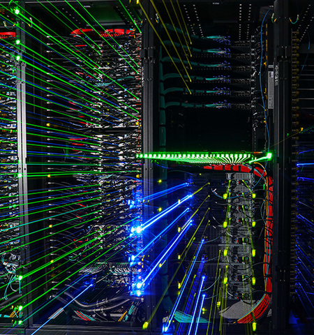 a photo of the inside of a supercomputer, which is dark with glowing blue, red, green and yellow streaming lights 
