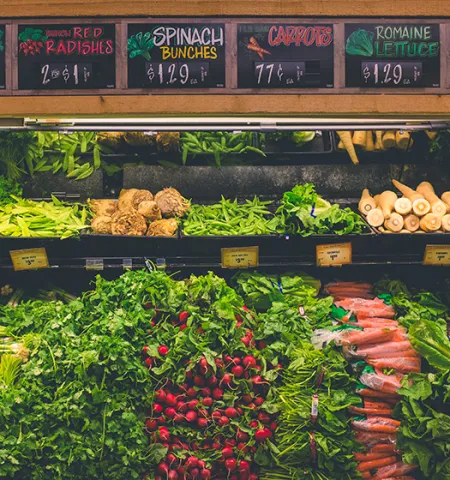 carrots, radishes, lettuce and other produce in a grocery refrigerated section with signs with names and prices for each product at the top