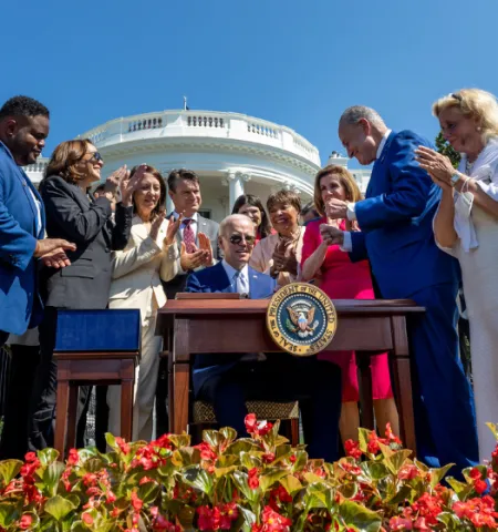 A group of men and women applaud as they stand round President Joe Biden after he signed the CHIPS and Science Act into law outside the White House.