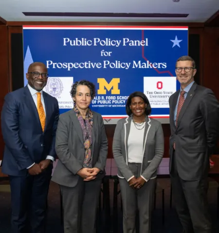 Two women and two men stand in front of a screen that reads “Public Policy Panel for Prospective Policy Makers”