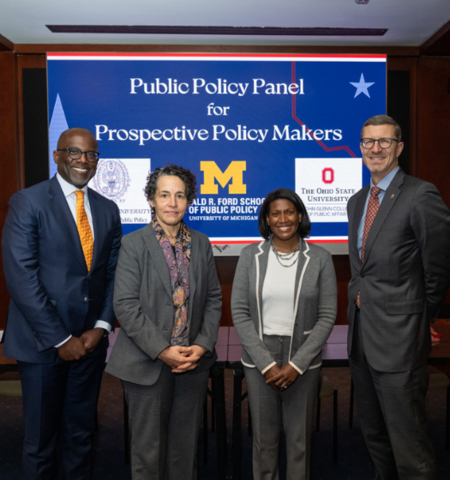 Two women and two men stand in front of a screen that reads “Public Policy Panel for Prospective Policy Makers”