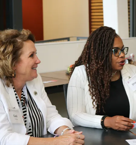 Two women sitting at a table; one woman is smiling and the other is talking.