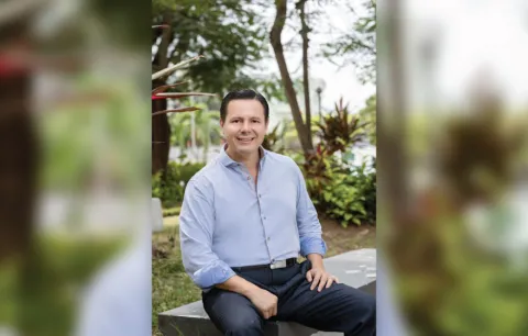 a man sits on a bench outside with tropical landscaping in the background