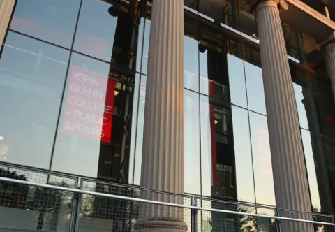 The two pillars of Page Hall and a red sign that reads John Glenn College of Public Affairs.