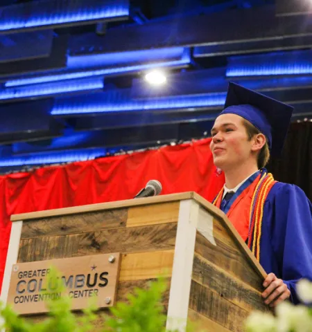 Josh Hickman standing at podium speaking into a microphone at graduation