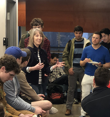 Elizabeth Newton stands and talks with a group of college students, some standing and some sitting, in the Battelle Center for Science, Engineering and Public Policy.