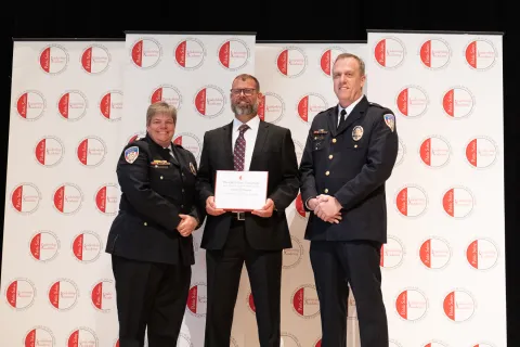 State officers congratulate and shake hands with a graduate of the Public Safety Leadership Academy as he holds his graduation certificate.