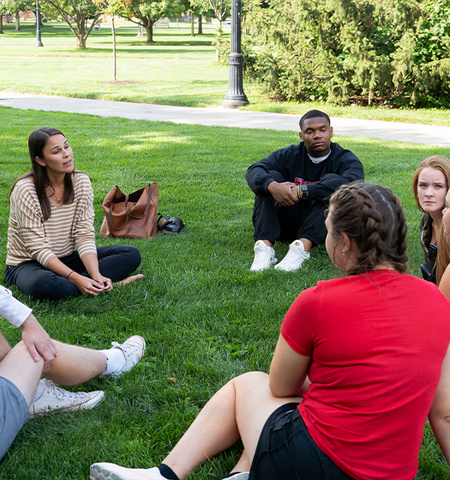 Professor sitting with students in the grass and having a conversation.