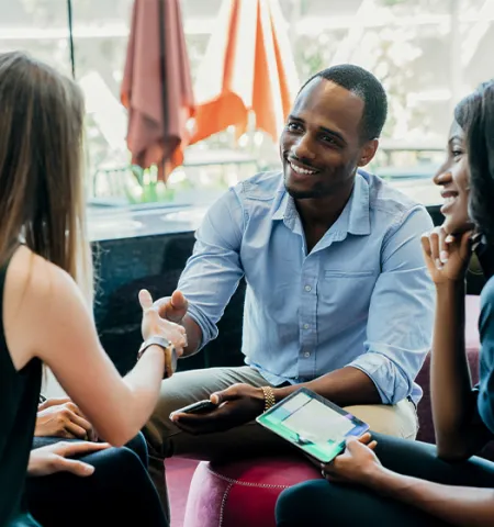 three women and a man sitting in a circle as the man and a women shake hands.