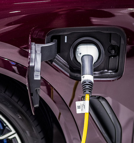 a fender of a dark maroon car with an electric charger cord plugged in