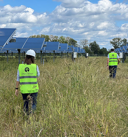 Two employees of Open Road Renewables, which supports work of the Ohio State EmPOWERment program led by John Glenn College of Public Affairs Associate Professor Jeffrey Bielicki, wear safety vests and hard hats as they walk away from the camera in a field of solar panels.