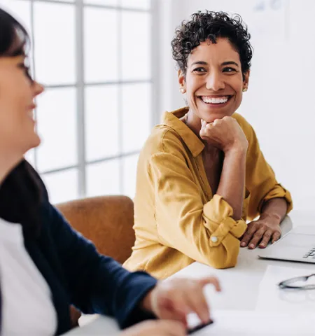 Two women sitting at a table; one woman is smiling and the other is talking.