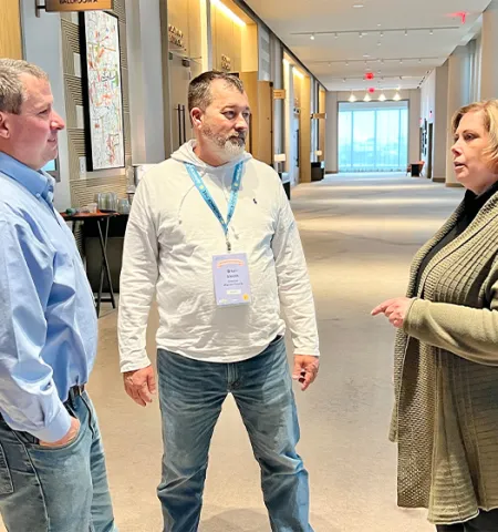 three people standing in a hallway talking.