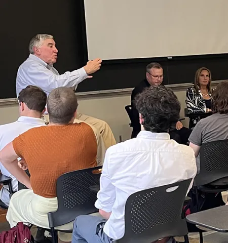 Glenn College Professor Ned Hill teaches in front of a classroom with guest panelists.