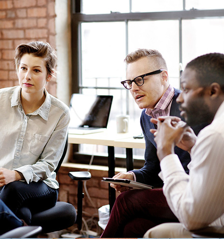 "A diverse group of four people having a focused discussion in a modern office with brick walls. They are seated in a circle, attentively listening to each other (Credit: AdobeStock.com).