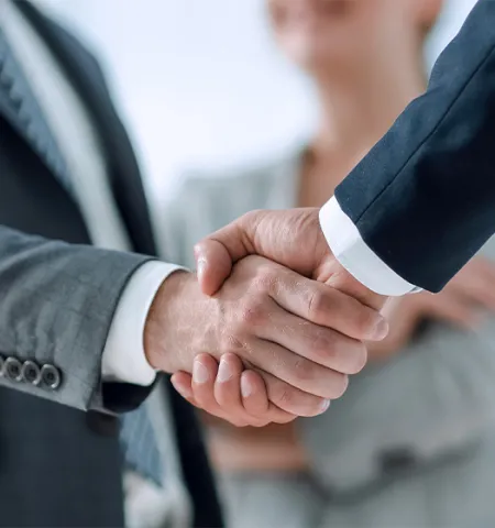 Two business professionals in suits shaking hands, with a third person in the background (Credit:AdobeStock.com).