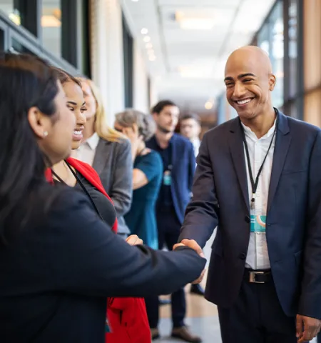 Male and female professionals are standing in a corridor shaking hands (Source: Getty Images).