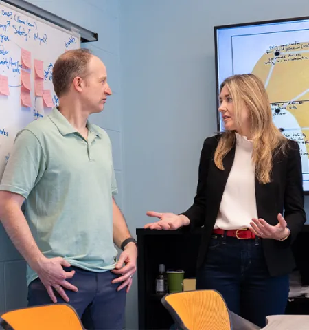 Ohio State Associate Professor Michael Rayo (left), Integrated Systems Engineering, and Glenn College Associate Professor Amanda Girth, Faculty Director, Washington Programs, stand in front of white boards with sticky notes and diagrams outlining their acquisition innovation research.