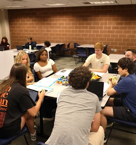 High school students sit around a table and draft financial plans for a fictional couple. 
