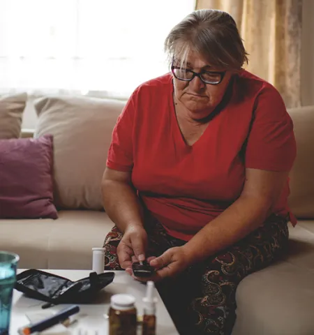 A woman seated on a couch checking her blood sugar in a living room