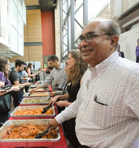 In Page Hall, faculty on the right side of a buffet table serve dinner to incoming graduate students on the left.