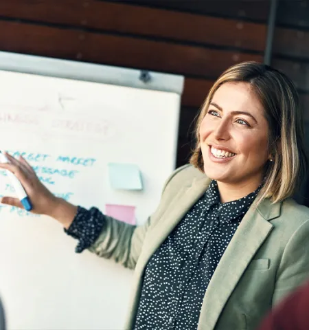 A happy woman planning and presenting information on a whiteboard to an audience (Source: AdobeStock).