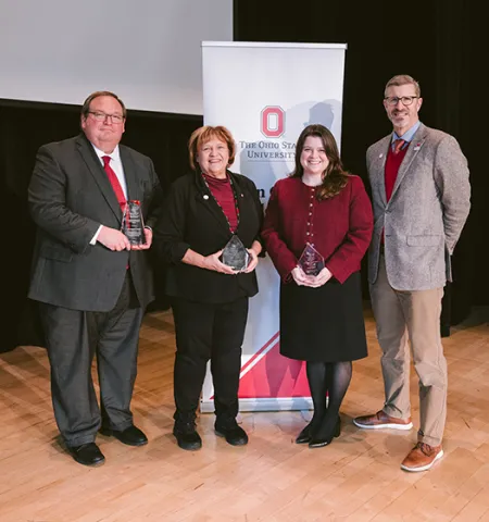 John Glenn College of Public Affairs Dean Trevor Brown (right) stands on a stage with the 2025 Alumni Award recipients (from left) Matthew Damschroder, Judith Zimomra and Mikayla Bodey