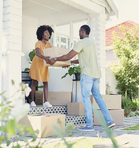 a man hands a moving box to a woman standing on the front porch of a home