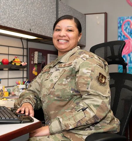 a woman in a camouflage uniform sits at a desk in front of a computer