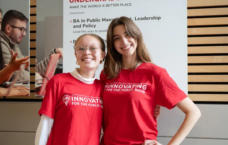Two girls pose in red shirts. They are smiling.